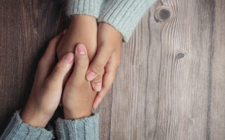 Two people holding hands together with love and warmth on wooden