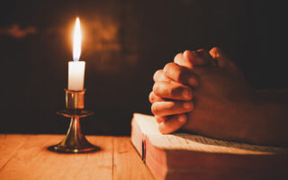 man praying on the Bible in the light candles selective focus