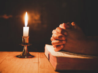 man praying on the Bible in the light candles selective focus